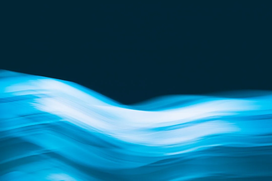 Close-up of a person cleaning a laptop screen with a blue cloth and spray cleaner, next to a houseplant.